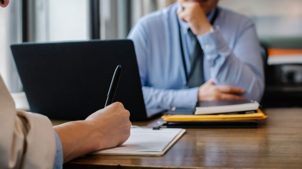 A junior recruiter working at an agency desk with a laptop and phone